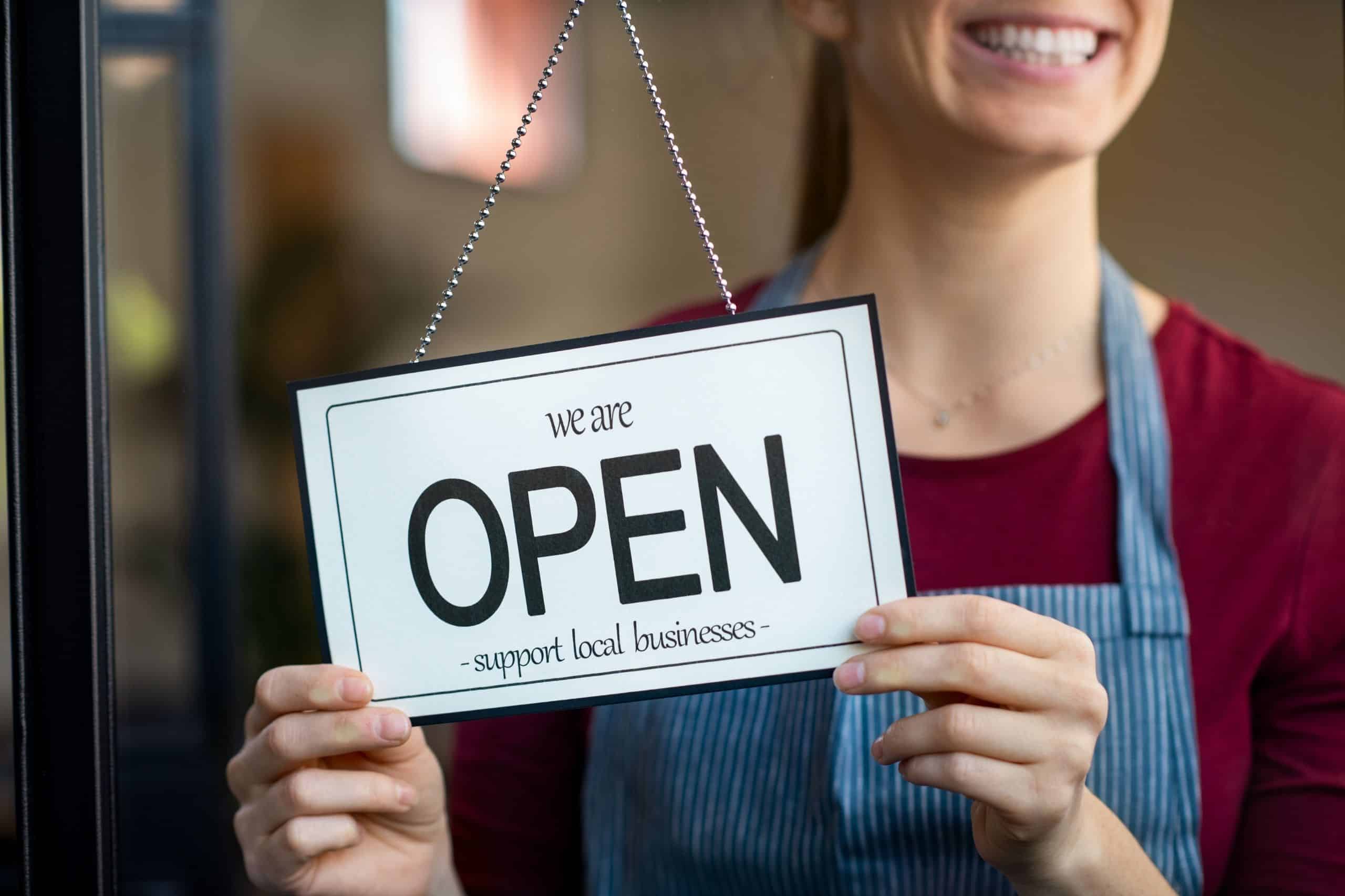 Local SEO Business Citations Services San Diego - woman holding a we're open, support local business sign - Ascendance Website Solutions