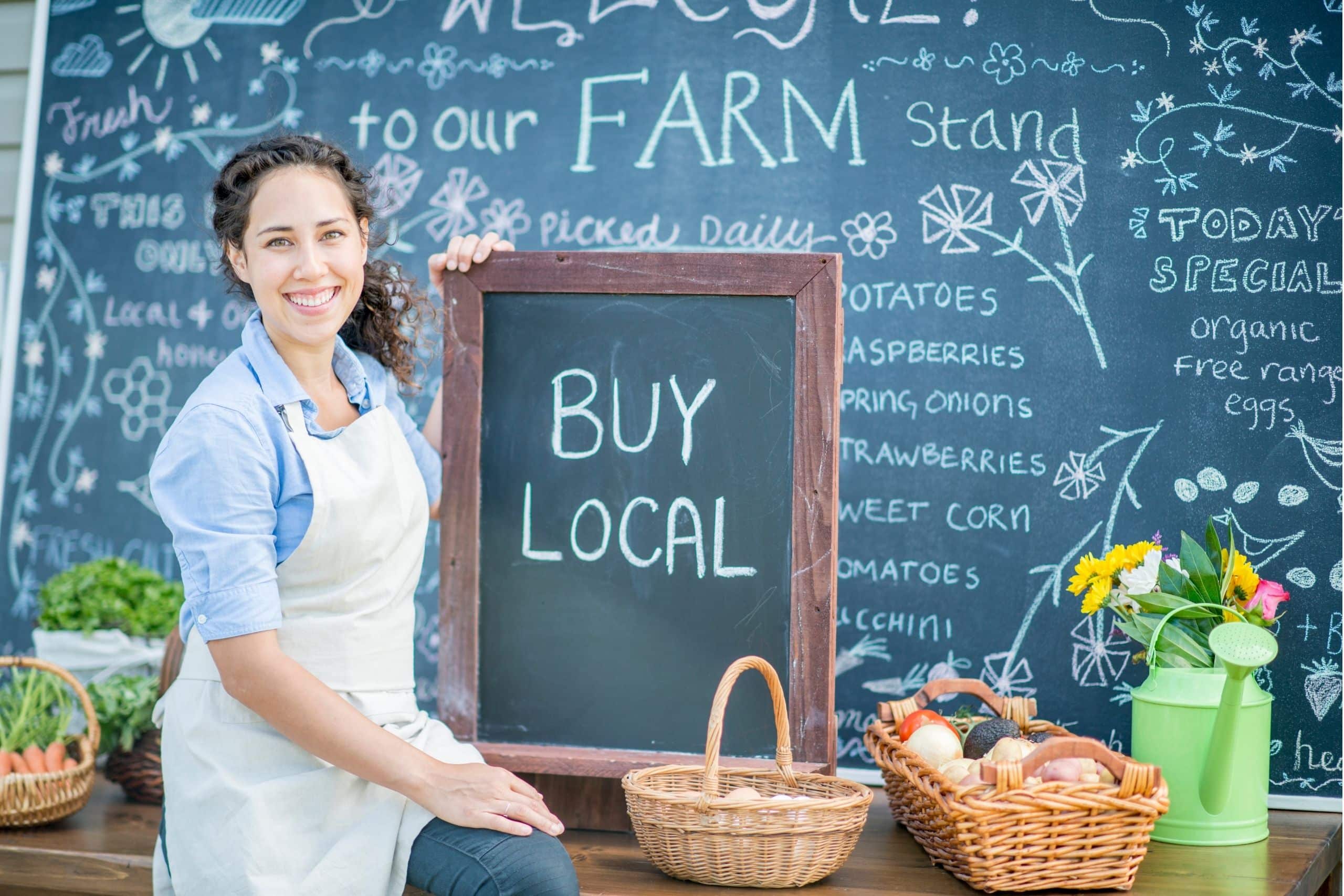 Local SEO Business Listings Services - woman with chalk board that says buy local surrounded by local farm goods - Ascendance Website Solutions